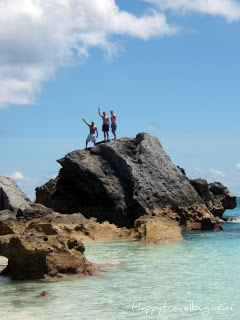 men waving from the top of a giant rock in the ocean