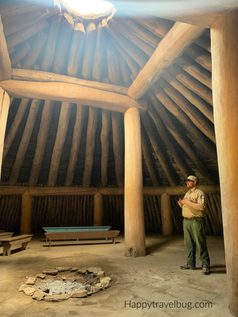 Inside the earth lodge with a park ranger. Large beams hold it together and the sun is shining through a hole in the top